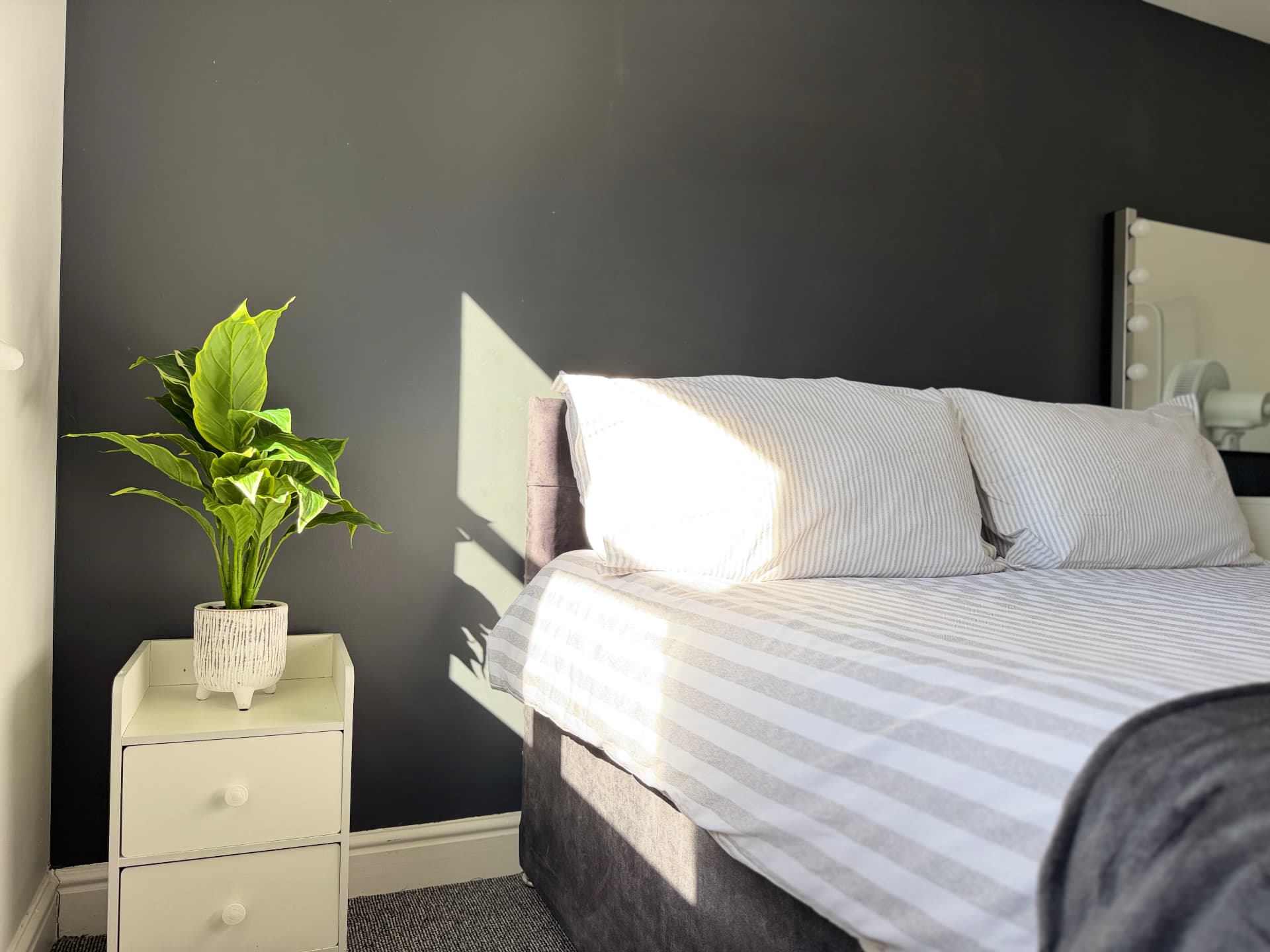 Century House sunlit king bedroom with striped bedding, bedside plant and dressing mirror